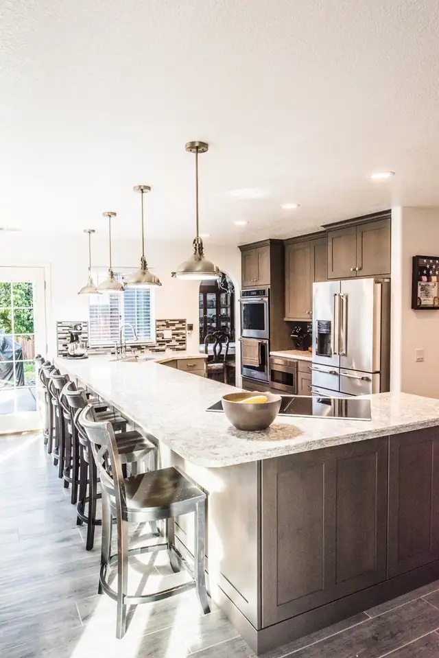 Long stained kitchen island with granite counter, bar seating and three pendant lights