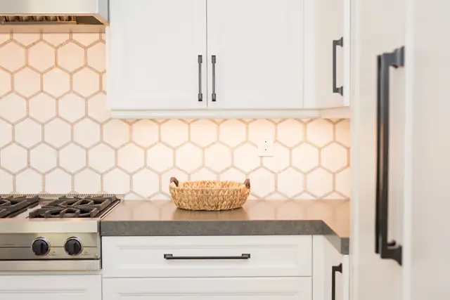White shaker cabinets over a honeycomb tile backsplash with gray counters and matte black pulls