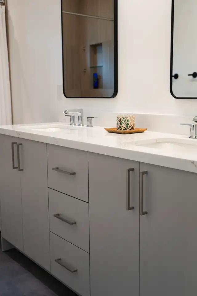 Bathroom remodel with a gray shaker double vanity, white quartz top and black-framed mirrors