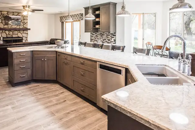 Mediterranean style kitchen with brown cabinets, a long granite counter, a stainless dishwasher and a stone fireplace beyond