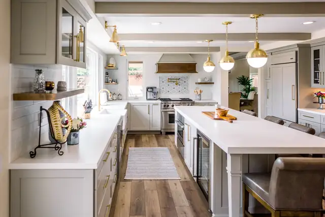 Kitchen with a long white island, gray leather stools, brass pendants and glass-front upper cabinets