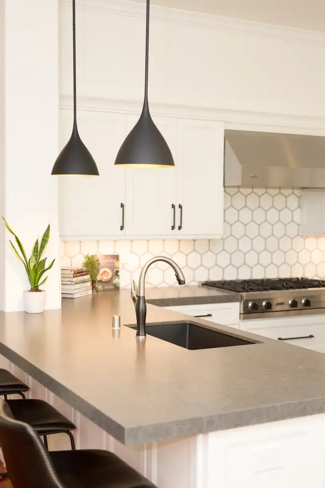 Kitchen peninsula with gray counter, undermount sink, black cone pendants and a honeycomb tile backsplash