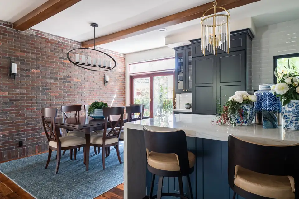 Navy island kitchen with waterfall quartz edge, leather counter stools, brass pendants and a brick dining wall, from Kitchen Barn's kitchen remodeling Poway portfolio