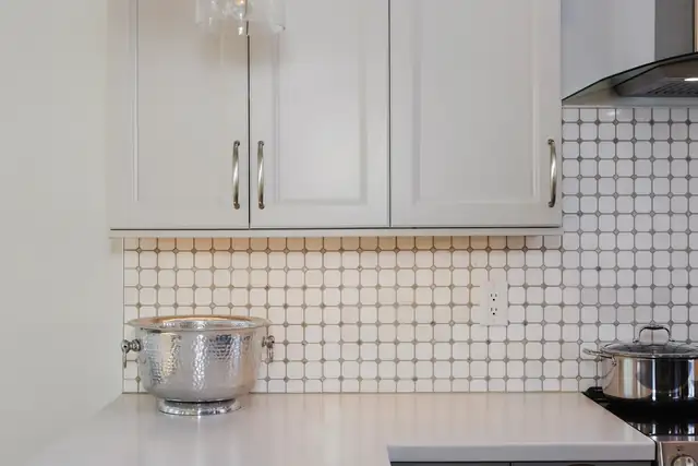 White kitchen cabinets above a dot-pattern tile backsplash and white quartz counter